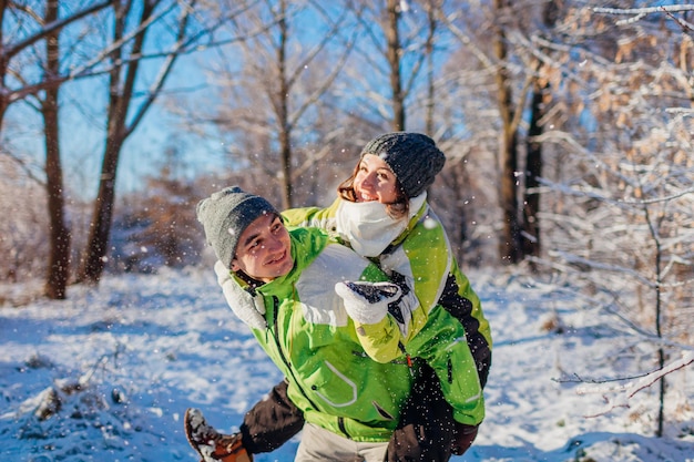 Mann gibt seiner Freundin Huckepack im Winterwald Verliebtes Paar hat Spaß