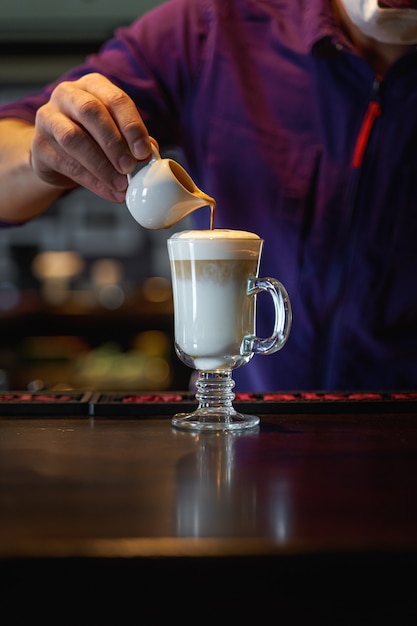 Mann gießt aufgeschäumte Milch in Espresso, der Latte-Kaffee macht. Hochformat