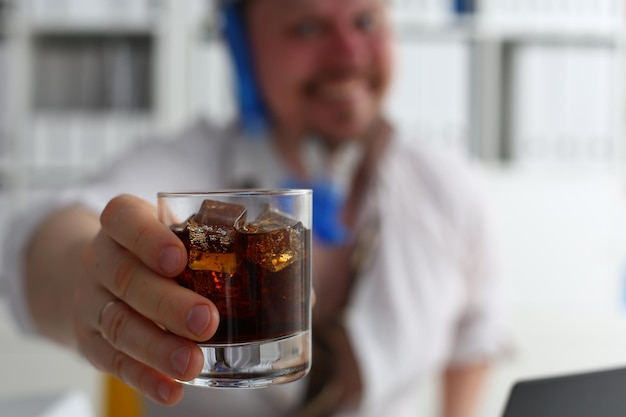 Mann hält am Arbeitsplatz im Büro ein Glas Cola und Whiskey mit Eis in der Hand