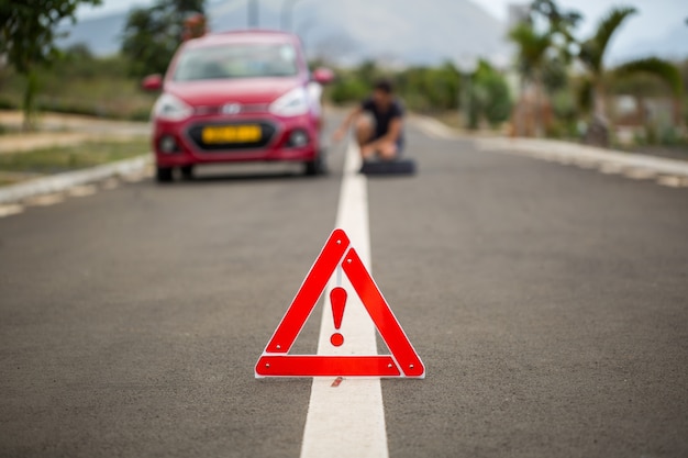 Mann hält das Reserverad gegen ein kaputtes Auto