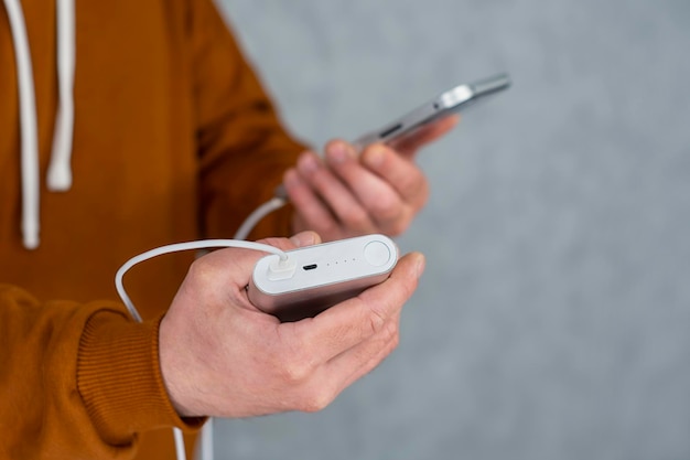 Mann hält ein Smartphone und ein tragbares Ladegerät in seinen Händen auf grauem Hintergrund Power Bank lädt das Telefon auf