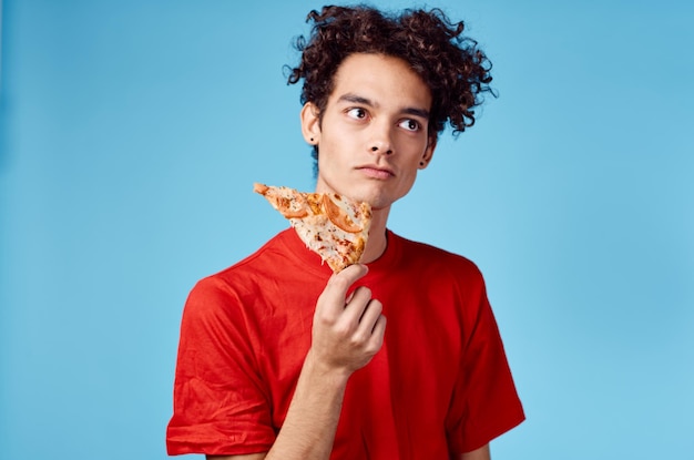 Mann hält ein Stück Pizza in der Hand und lockiges Haar, rotes T-Shirt, blauer Hintergrund