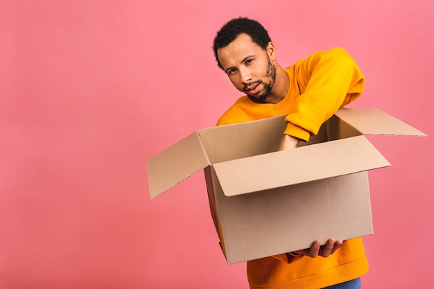 Mann hält eine leere Box isoliert über rosa. Lieferkonzept.