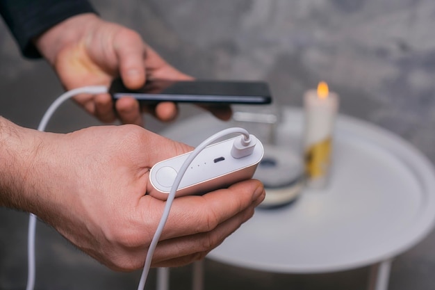 Mann hält eine Powerbank in den Händen und lädt ein Smartphone gegen eine Betonwand auf