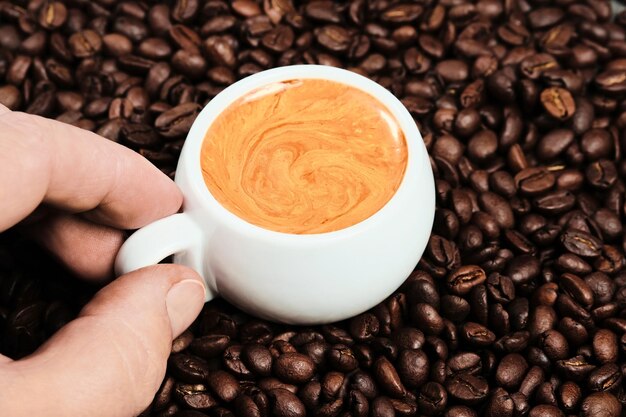 Mann hält eine Tasse Espressokaffee, Draufsicht, Nahaufnahme auf der Tasse. Weiße Tasse mit Espressokaffee und Kaffeebohnen im Hintergrund. Italienischer Kaffee zum Frühstück