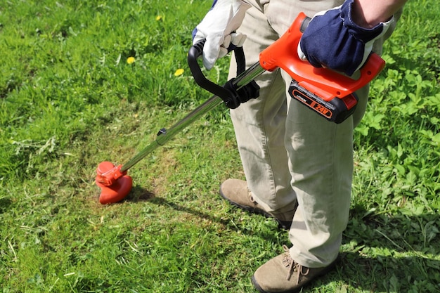 Mann hält elektrischen Trimmer in seinen Händen und mäht Gras auf der Wiese