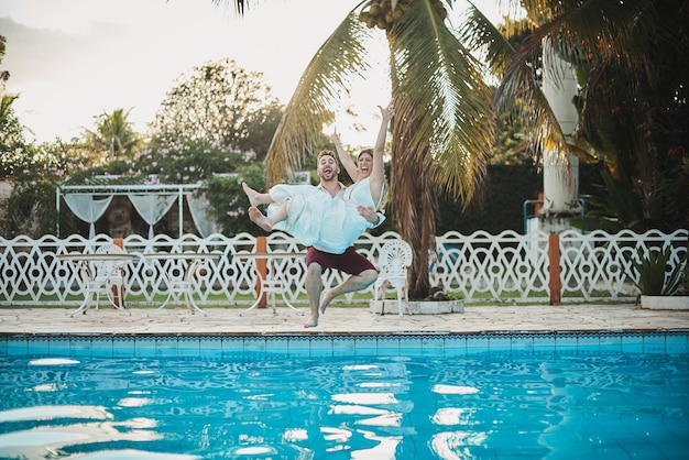 Mann hält Frau auf seinem Schoß und springt in den Pool