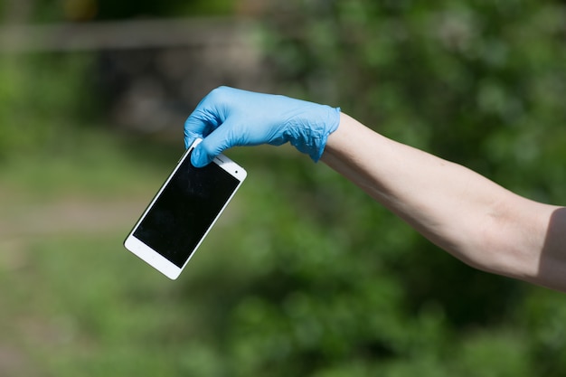 Mann hält Handy in Händen in medizinischen Handschuhen.