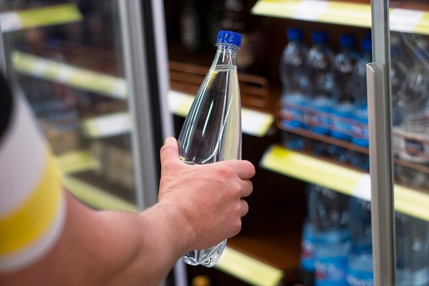 Mann hält in der Hand eine Plastikflasche mit reinem Mineralwasser auf dem Hintergrund eines Schaufensters.