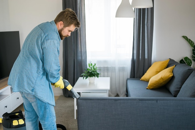 Foto mann hält modernen waschstaubsauger und reinigt schmutziges sofa mit professionellem reinigungsmittel prof