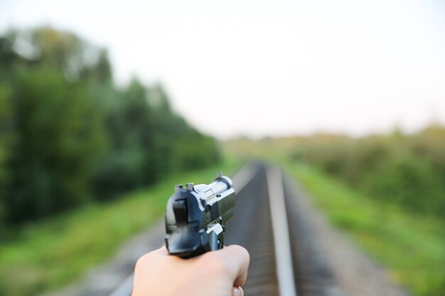 Mann hält Pistole in der Hand. Kriminelles Konzeptfoto. Bahngleise im Hintergrund.