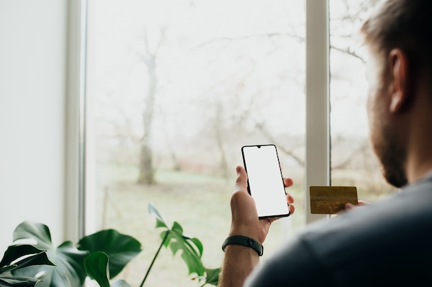 Mann hält Smartphone mit weißem Bildschirm und Bankkarte.