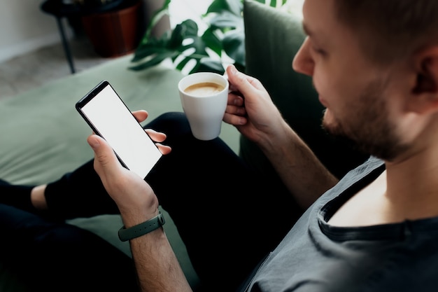 Mann hält Smartphone mit weißem Bildschirm und Kaffeetasse.