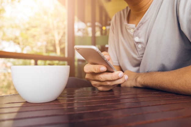 Mann hält Telefon mit einem Kaffee auf dem Holztisch