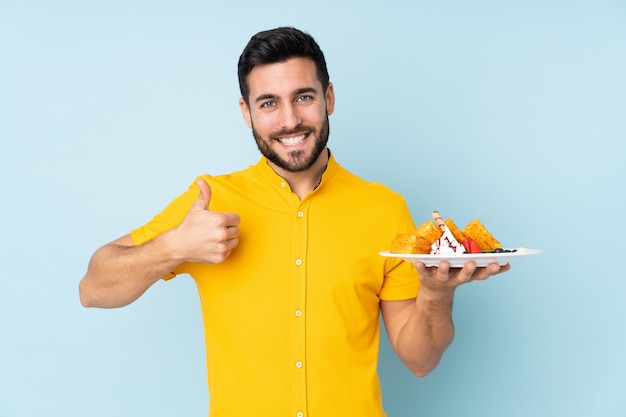 Mann hält Waffeln auf Blau mit Daumen hoch, weil etwas Gutes passiert ist