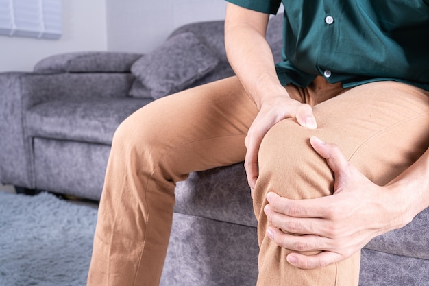 Foto mann hand hält knie schmerzen beim sitzen auf dem sofa.