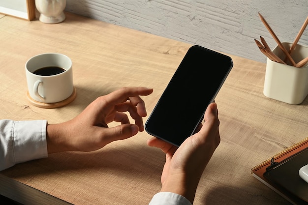 Mann Hand hält Smartphone über Schreibtisch aus Holz Nahaufnahme leerer Bildschirm für Ihre Werbung