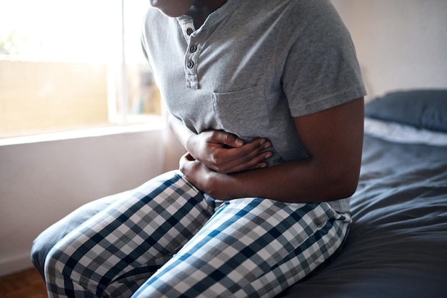 Foto mann hat bauchschmerzen und hände halten sich morgens den bauch in einem schlafzimmer in einem haus. ein afrikanischer mann ist krank und hat verdauungsschmerzen in einem haus auf einem bett und fühlt sich verletzt, mit bauchkrämpfen und ibs-problemen