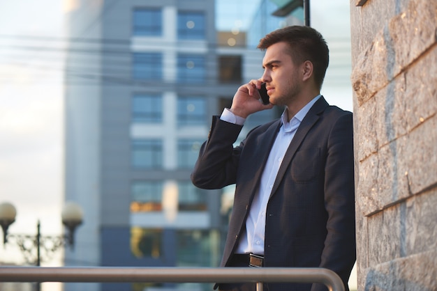 Mann im Anzug telefoniert mit dem Handy gegen das Gebäude mit Glasfassade