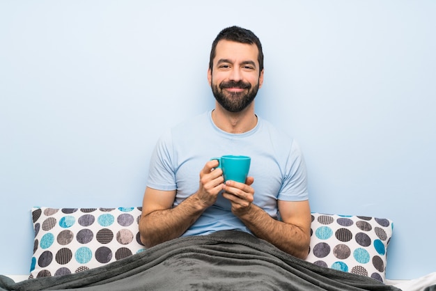 Mann im Bett mit dem Bart, der einen Tasse Kaffee hält