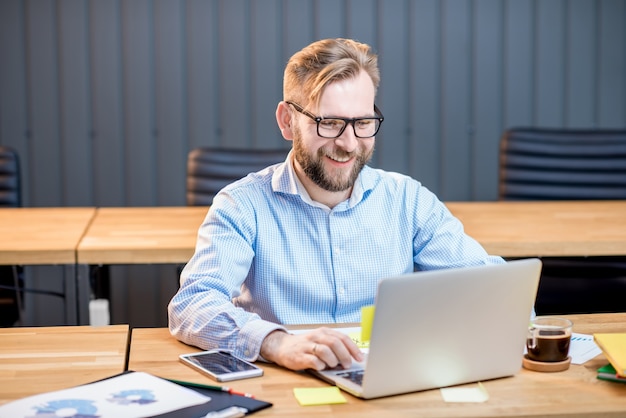 Mann im blauen Hemd, der mit Laptop im modernen Bürointerieur arbeitet