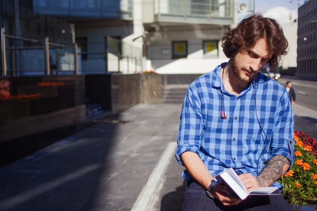 Mann im blauen Hemd liest ein Buch. Porträt des jungen gutaussehenden stilvollen Mannes auf der Straße.