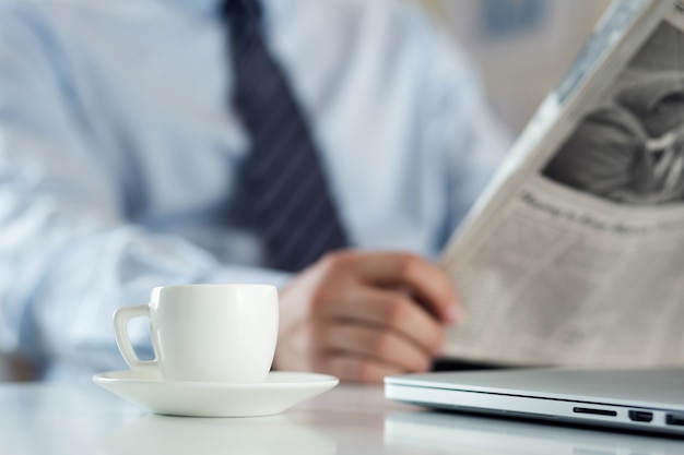 Mann im Büro, der Zeitung liest und Kaffee trinkt