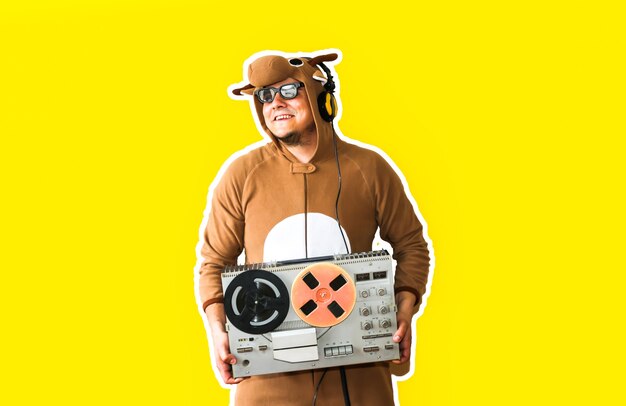 Mann im Cosplay-Kostüm einer Kuh mit Reel-Tonbandgerät isoliert auf gelbem Hintergrund. Kerl in der Tierpyjamanachtwäsche. Lustiges Foto mit Partyideen. Disco-Retro-Musik.