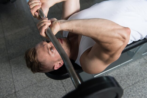 Mann im Fitnessstudio Trizeps mit Langhantel trainieren