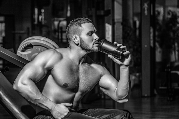 Mann im Fitnessstudio und hält eine Flasche Wasser in der Hand. Lifestyle-Porträt eines gutaussehenden, muskulösen Mannes, der im Fitnessstudio Wasser trinkt, Schwarz-Weiß