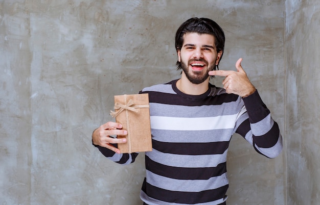 Mann im gestreiften Hemd hält eine Geschenkbox aus Karton und lächelt