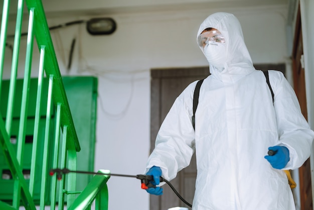 Mann im Hazmat-Anzug desinfiziert den Eingang eines Wohnhauses.