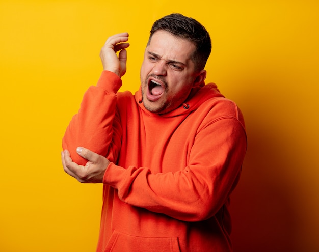 Mann im Hoodie mit den Schmerz im Ellbogen auf gelber Wand