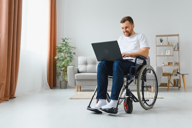 Mann im Rollstuhl arbeitet am Laptop im Wohnzimmer