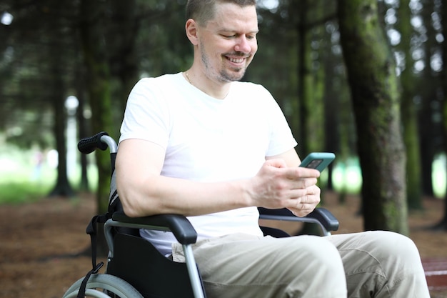 Mann im Rollstuhl sitzt mit Smartphone in der Hand und lächelt