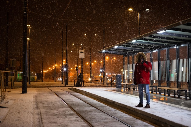 Mann im roten Wintermantel, der an der Straßenbahnhaltestelle steht und auf öffentliche Verkehrsmittel wartet