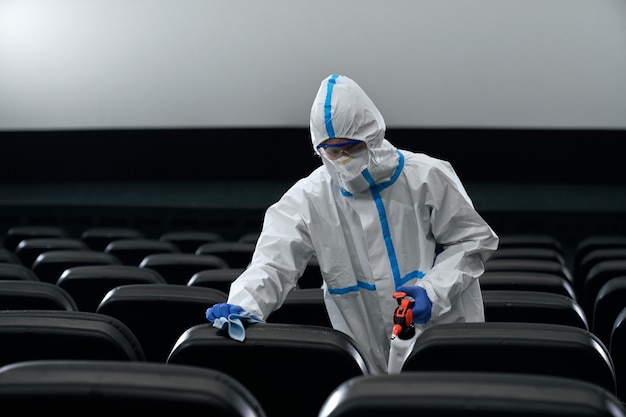Mann im Schutzanzug desinfizieren Kinosaal