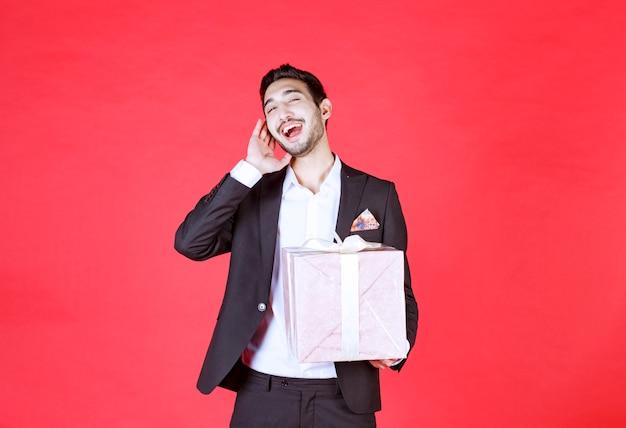 Mann im schwarzen Anzug, der eine lila Geschenkbox hält und schreit.