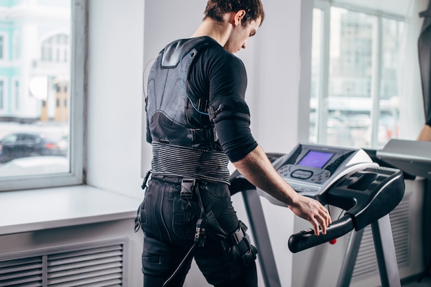 Mann im schwarzen Anzug für ems Training auf dem Laufband