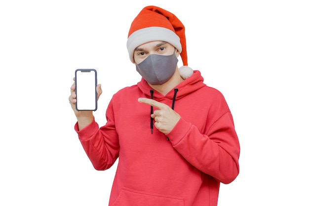 Mann im Weihnachtshut mit einem Handy und einer Maske als Symbol der Feier Weihnachten 2020 in Pandemiezeiten.