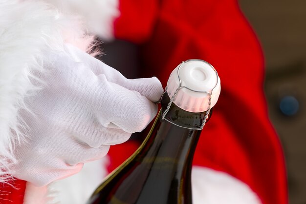 Foto mann im weihnachtsmannkostüm öffnet eine flasche champagner