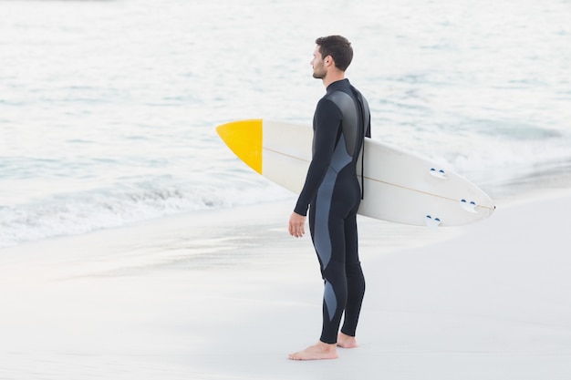 Mann im Wetsuit mit einem Surfbrett an einem sonnigen Tag