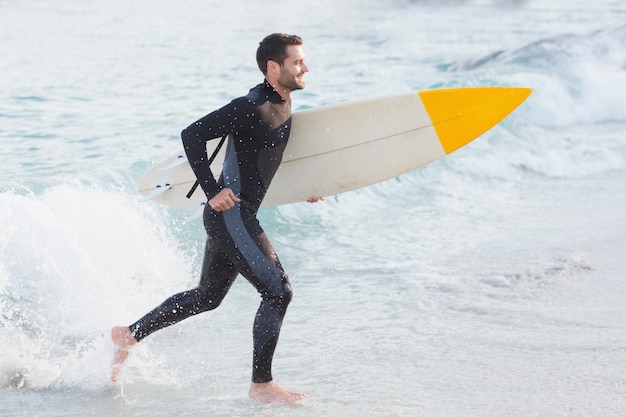 Mann im Wetsuit mit einem Surfbrett an einem sonnigen Tag