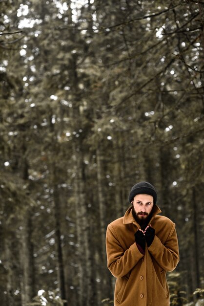 Mann im Winterwald ist kalt und in einem braunen Mantel und Handschuhen