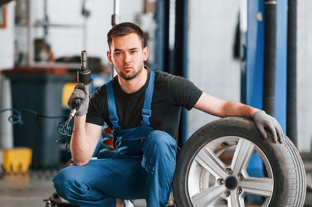 Mann in Arbeitsuniform sitzt mit Autorad drinnen Konzeption des Automobilservices