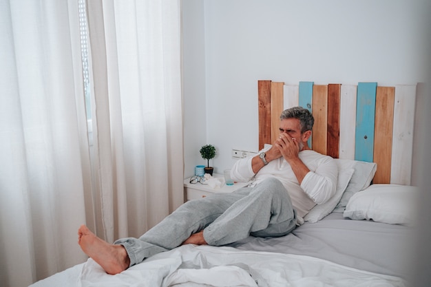 Mann in den 50ern mit grauen Haaren, der sich in seinem Bett erkältet hat