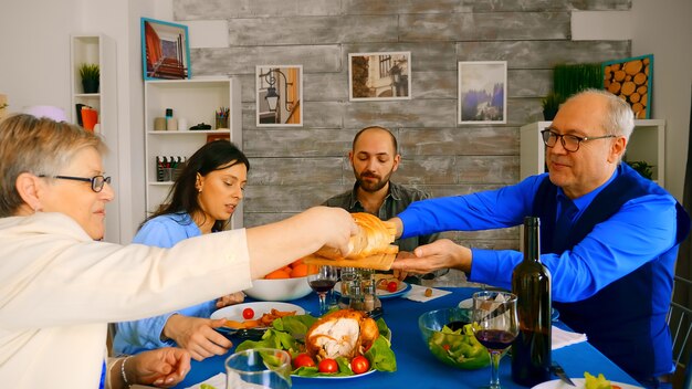 Mann in den Sechzigern, der seiner Frau beim Familienessen Brot serviert.