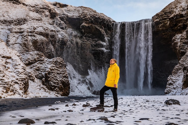 Mann in der gelben Jacke auf dem Hintergrund des Wasserfalls Skogafoss im Winter im Morgengrauen Einer der beliebtesten Orte in Island