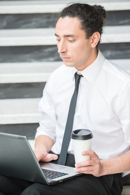 Mann in der klage, die an der treppe im büro sitzt und laptop verwendet.