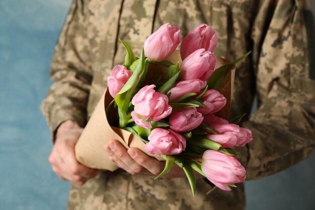 Mann in der Militäruniform, die Strauß Tulpen auf Blau, nah oben hält